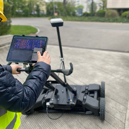 Worker operating a ground penetrating radar in a paved outdoor area
