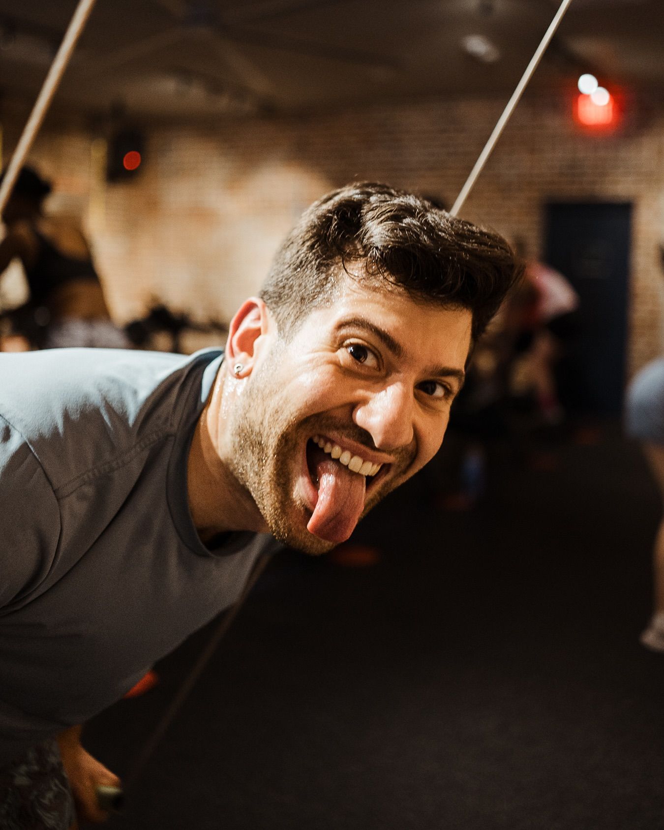 Smiling man leaning toward camera and sticking out his tongue in a dim indoor setting