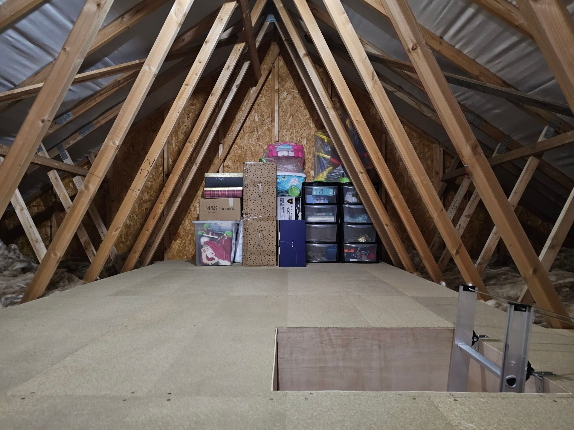loft boarding with wooden beams, storage boxes, and a ladder by the access opening.
