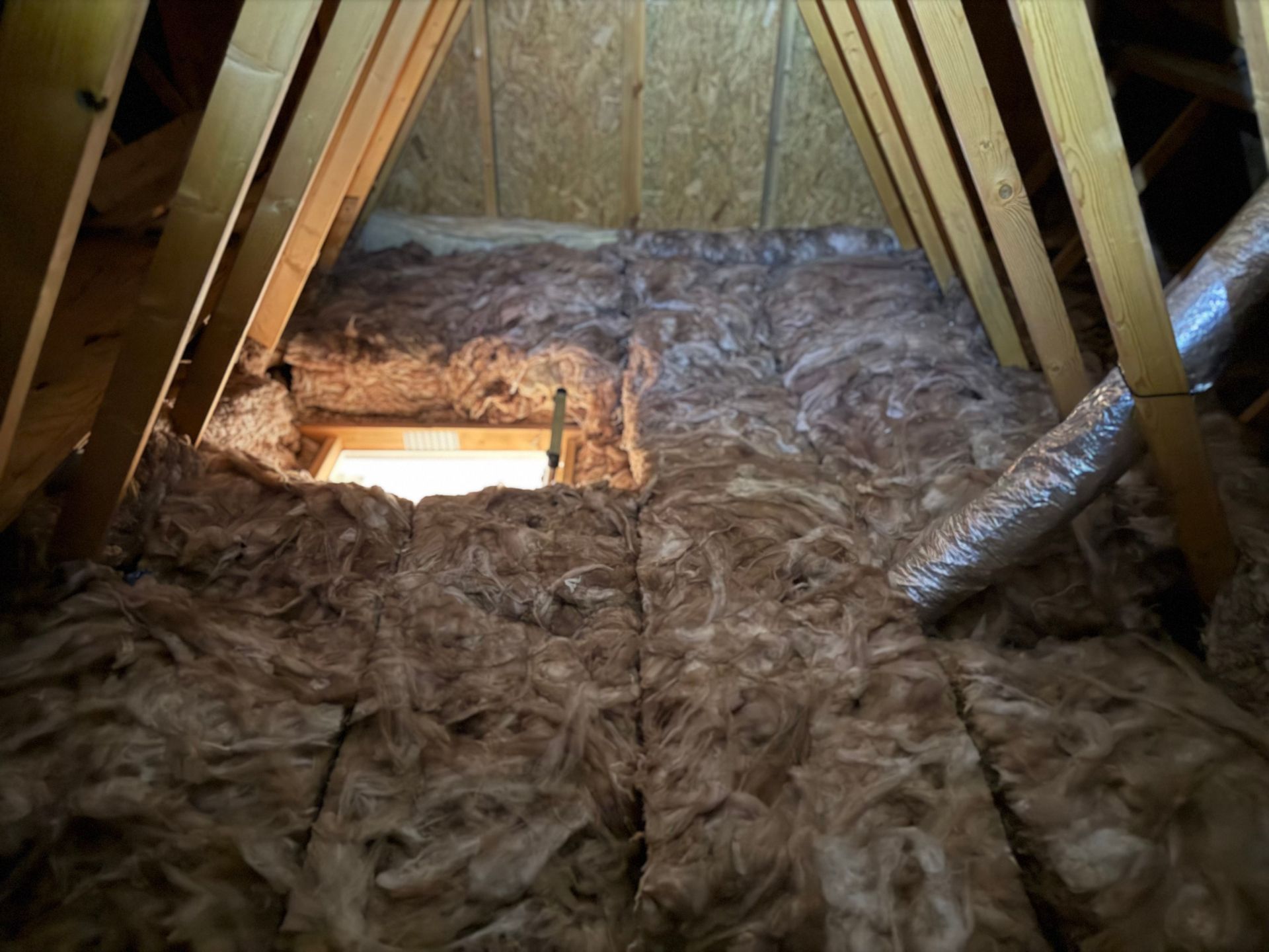 Person in protective suit cuts insulation in an Loft, with a roll of insulation nearby.