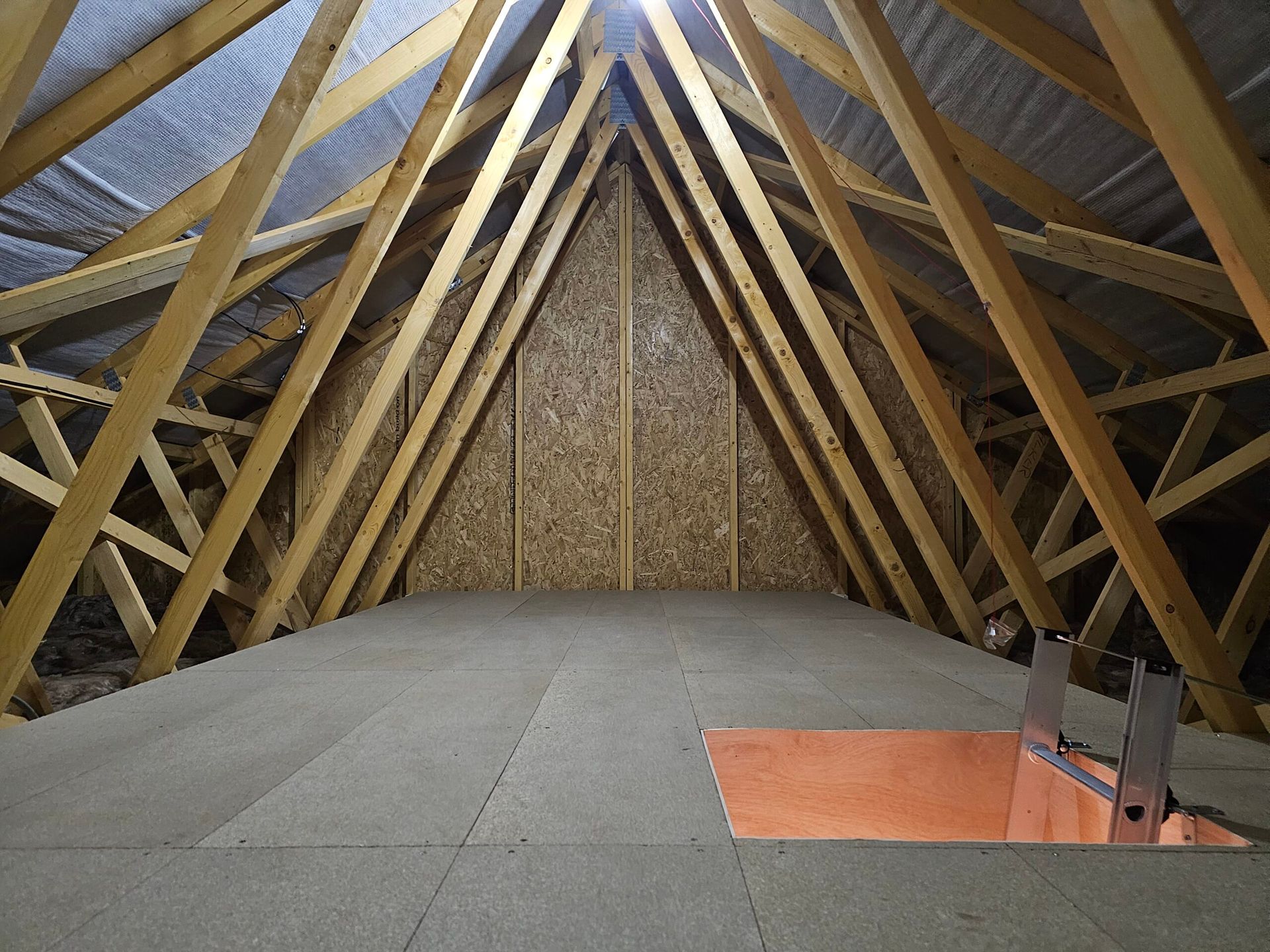 Interior view of an Loft with wooden beams, a partially floored area and an access hatch.