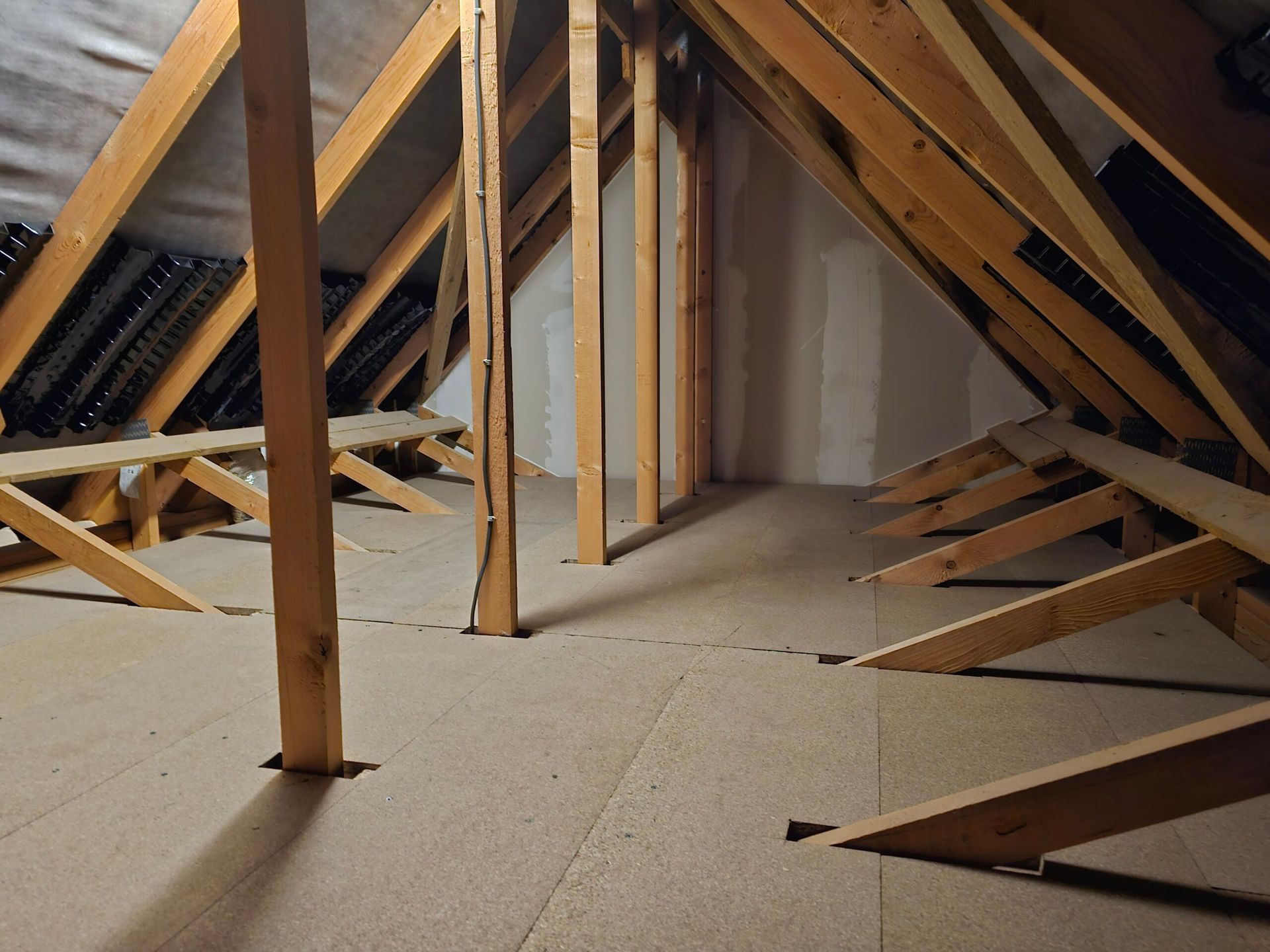 Loft interior with exposed wooden beams, insulation, and partial flooring; a potential storage space.