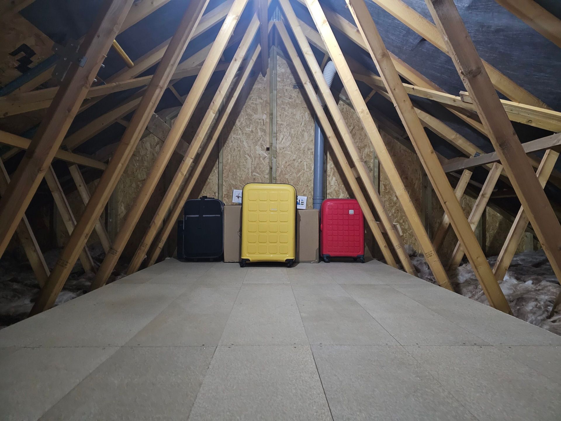 Suitcases in an attic. Wooden beams frame a red, yellow, and black suitcase on a floored surface.