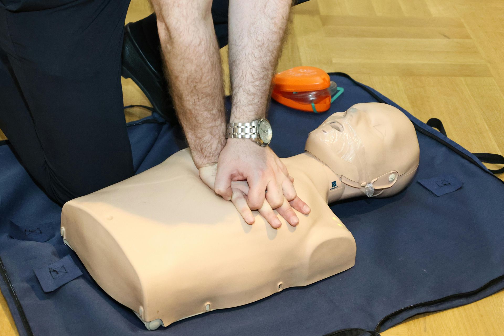 Person practicing CPR chest compressions on a training manikin on a mat