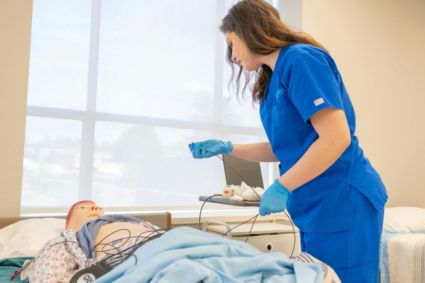 Nurse in blue scrubs checks a patient lying in a hospital bed beside medical equipment.