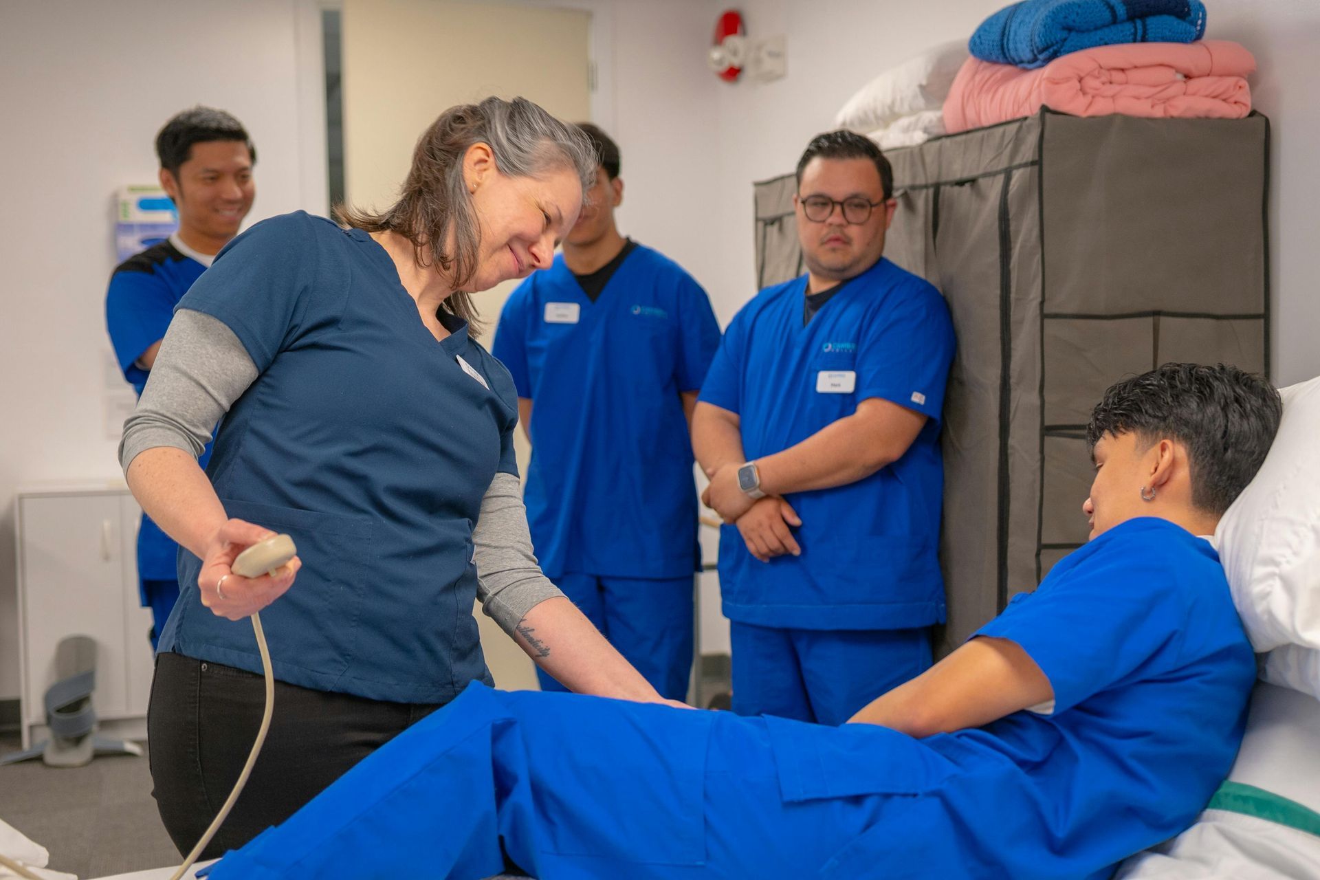 Medical staff in blue scrubs tending to a patient on a bed in a clinical room