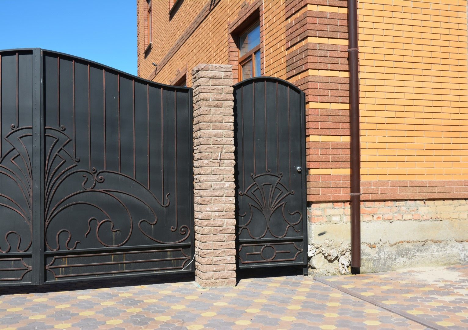 Black wrought-iron gate and smaller door next to a brick building with a stone pillar.