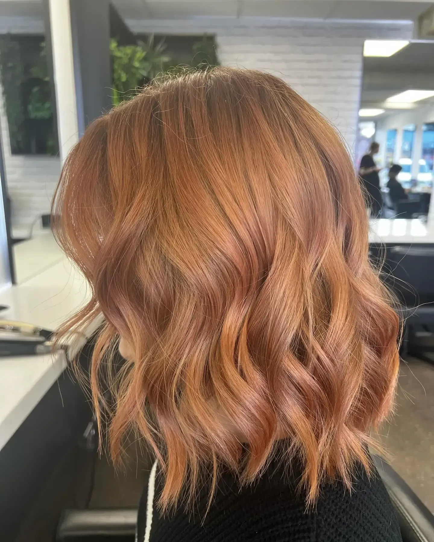 Wavy copper-blonde shoulder-length bob hairstyle in a salon setting, shown from the side.