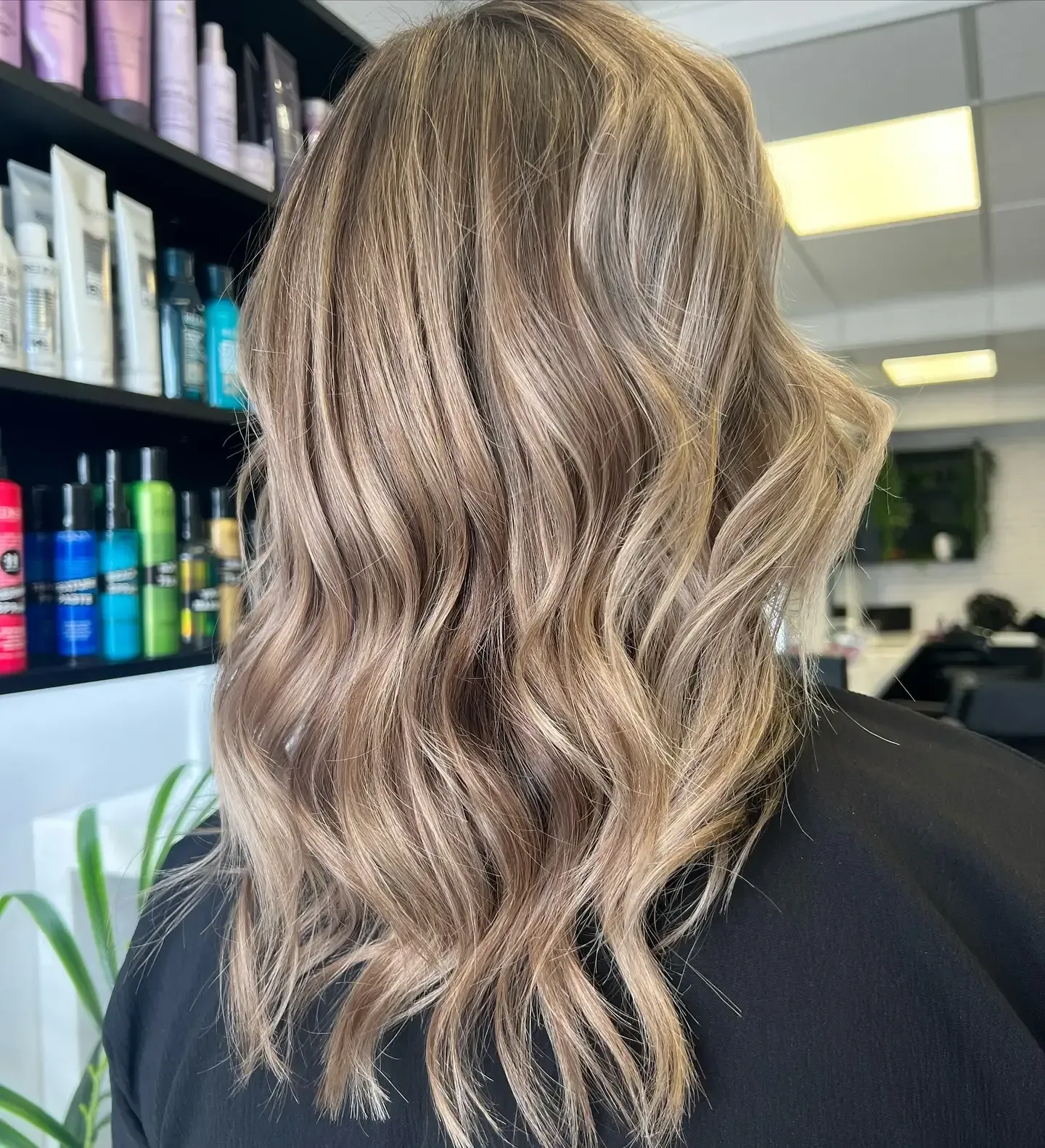Wavy, shoulder-length blonde balayage hair viewed from the back in a salon.