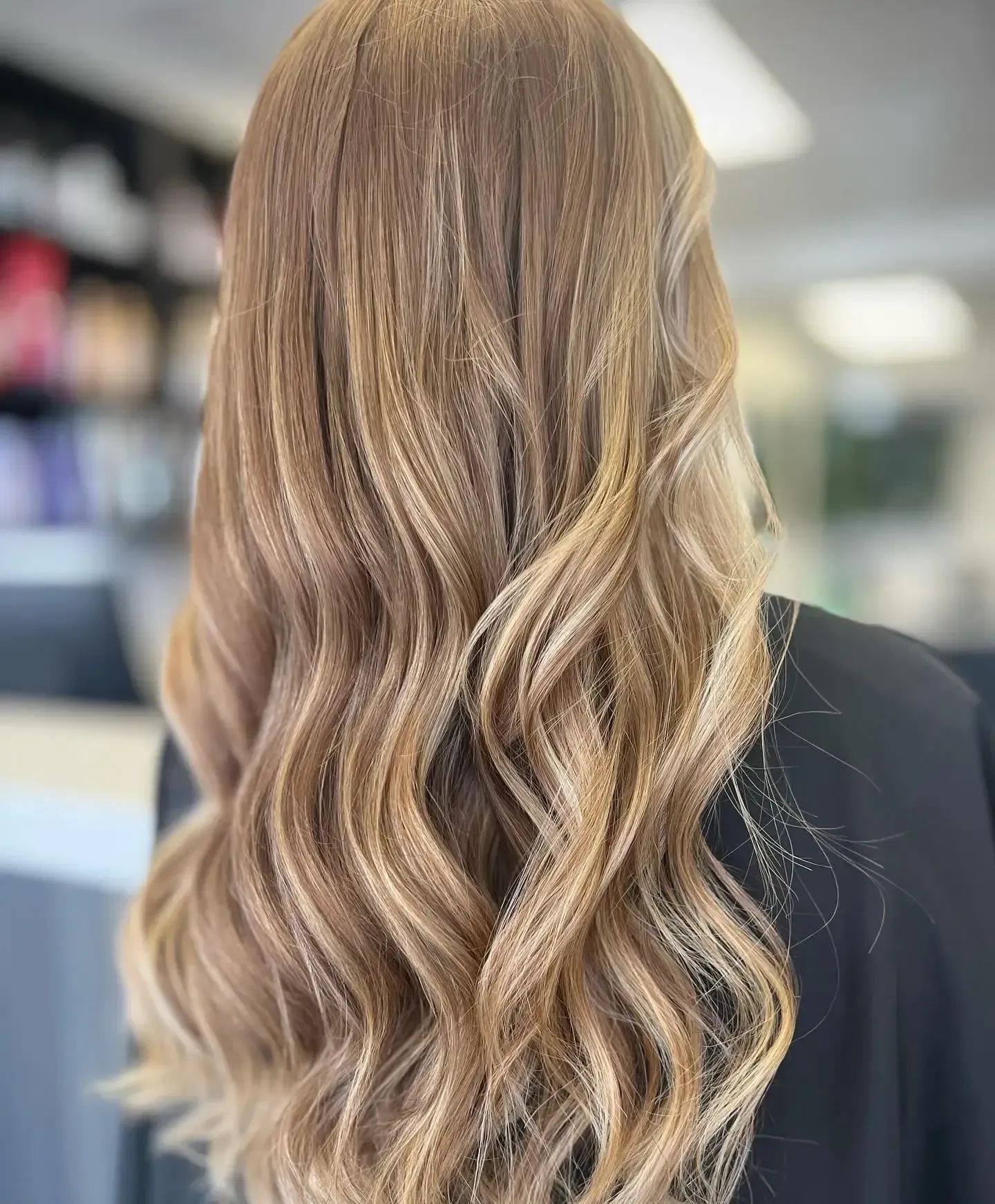 Wavy blonde balayage hair styled down, shown from the back in a salon