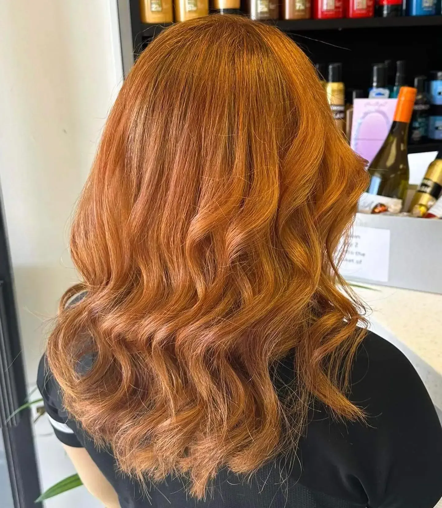 Wavy copper-red hair styled in layers, viewed from behind in a salon setting