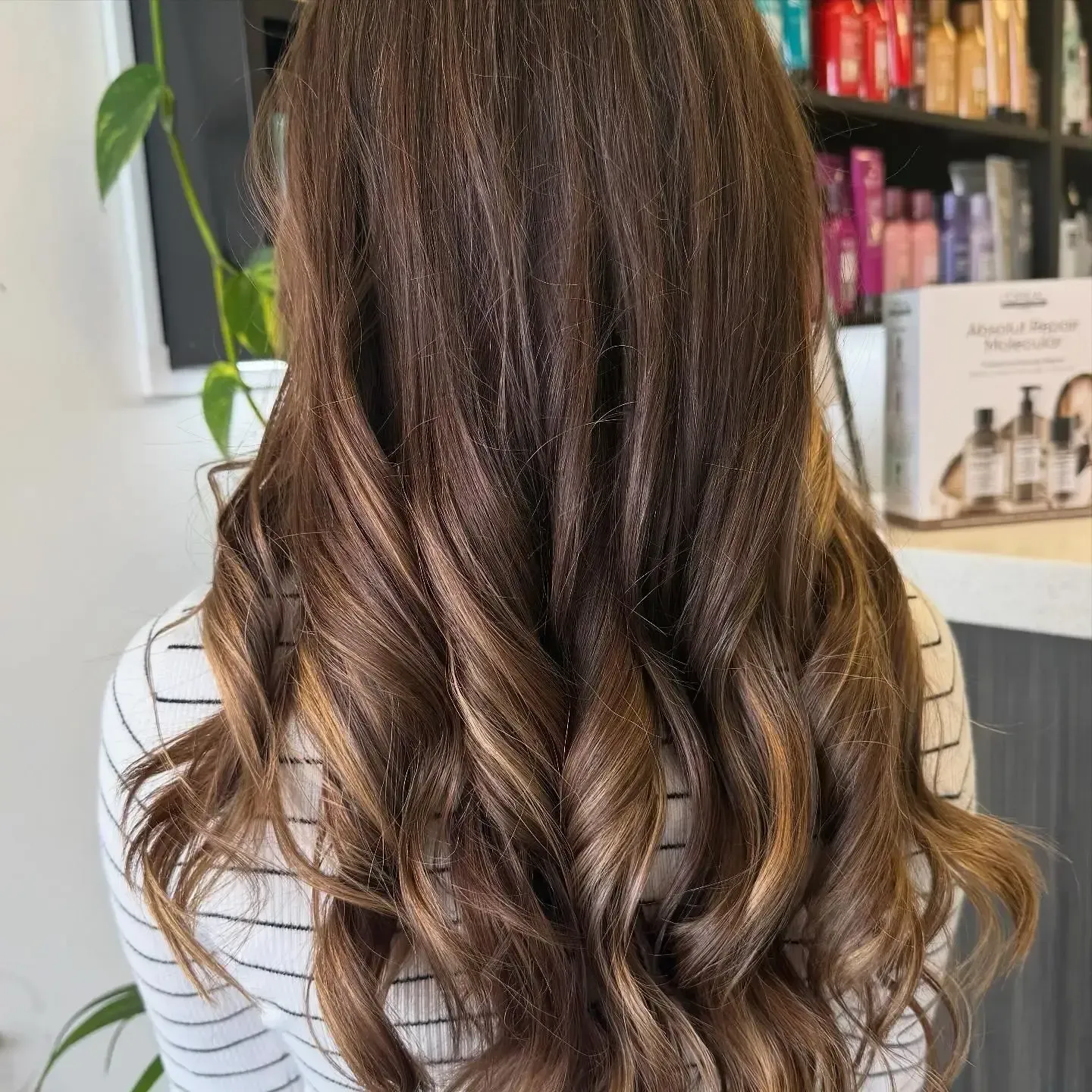 Long wavy brown hair with light highlights, shown from the back in a salon setting