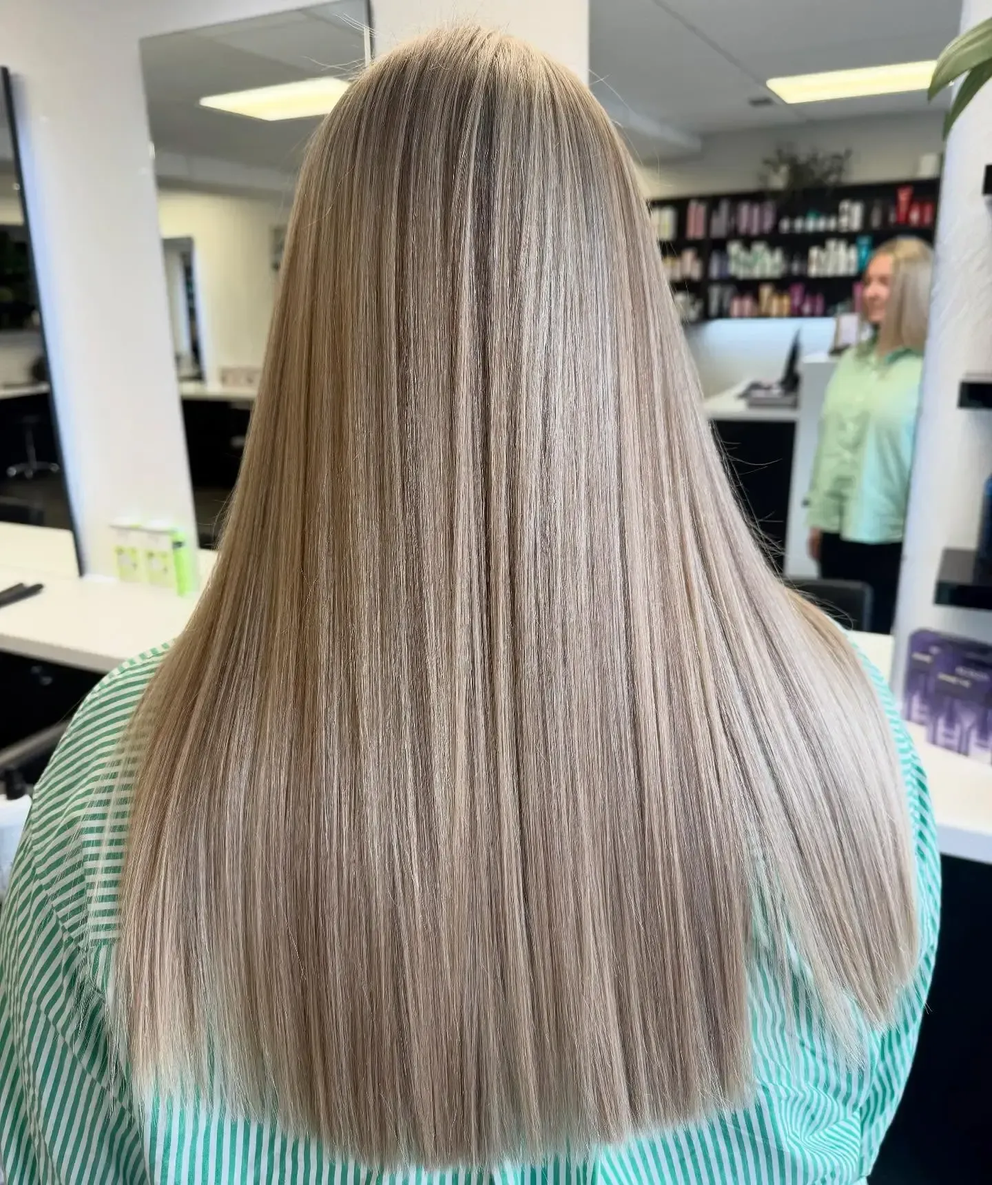 Long straight blonde hair viewed from behind in a salon mirror.