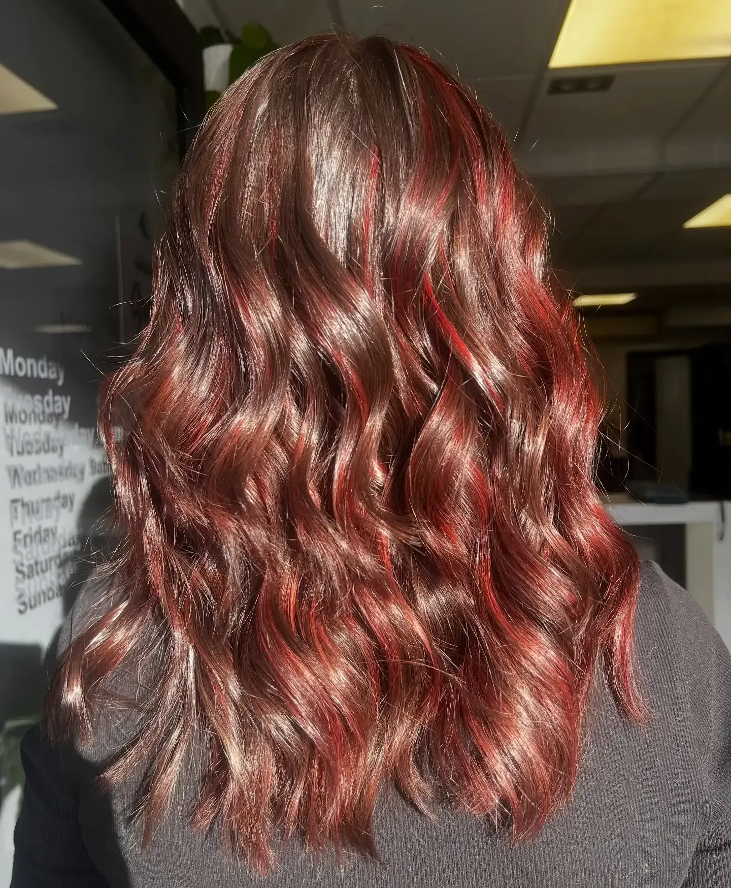 Back view of wavy shoulder-length hair with reddish highlights in a salon setting