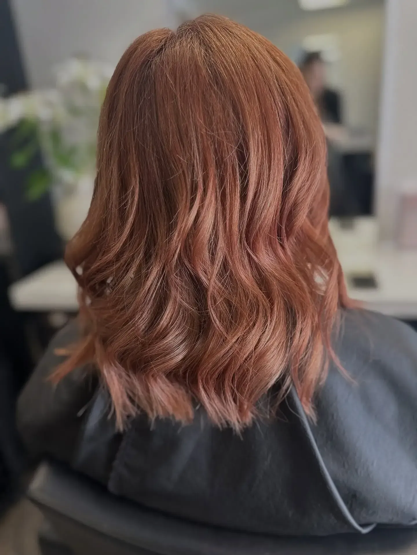 Wavy copper-brown shoulder-length hair viewed from behind in a salon chair