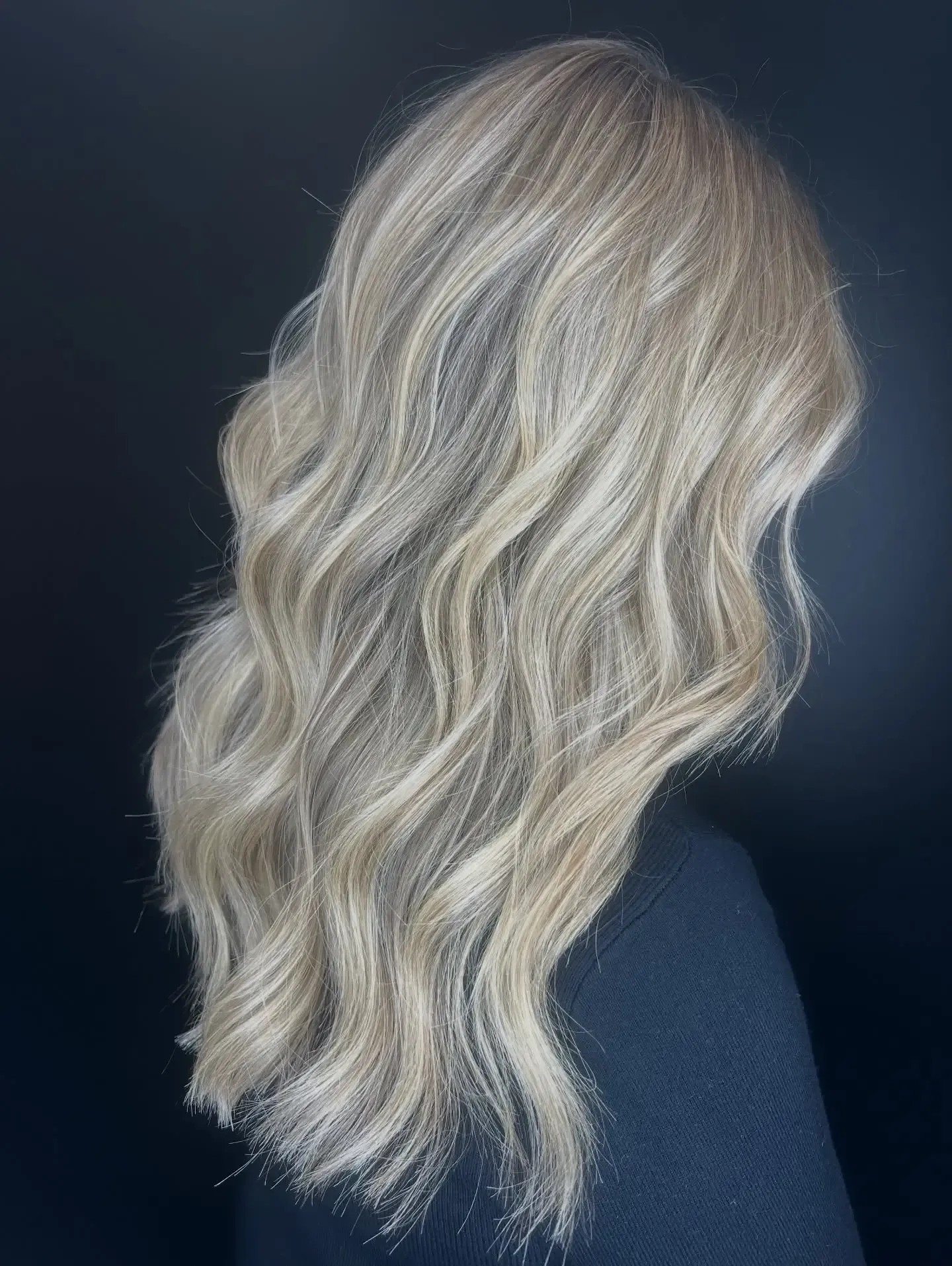 Wavy blonde hair in a shoulder-length style against a dark background