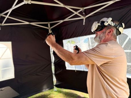 Person playing VR inside a black tent, wearing a beige shirt and headphones.