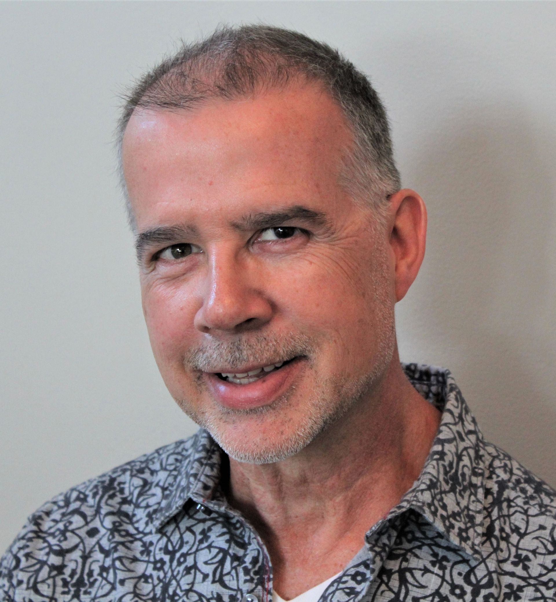Smiling person in a patterned shirt against a plain light wall