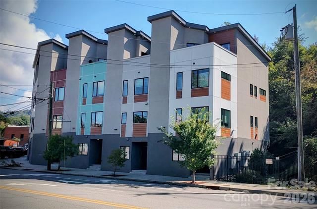 Modern four-story apartment building with white, gray, and blue facade beside a street