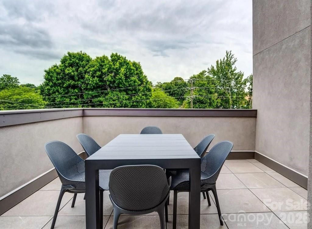Outdoor patio with dark table and four chairs beside a concrete wall, overlooking green trees under cloudy sky