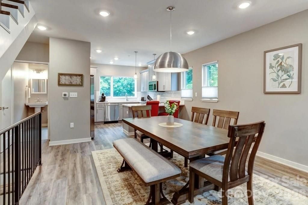 Bright modern dining room with wooden table, bench, chairs, pendant light, and kitchen in background
