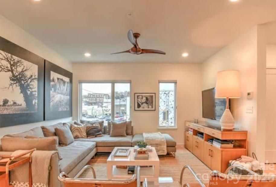 Bright living room with beige sectional, TV console, wall art, and large windows overlooking a view.