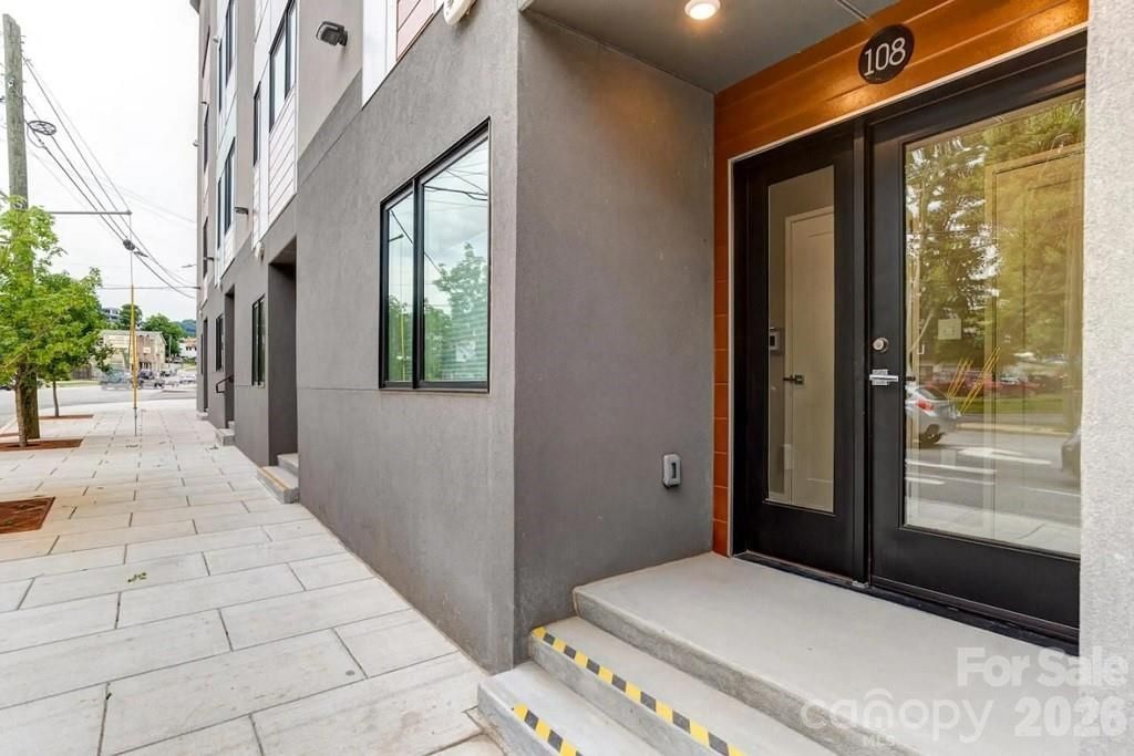 Modern gray building entrance with glass door and sidewalk steps on a city street