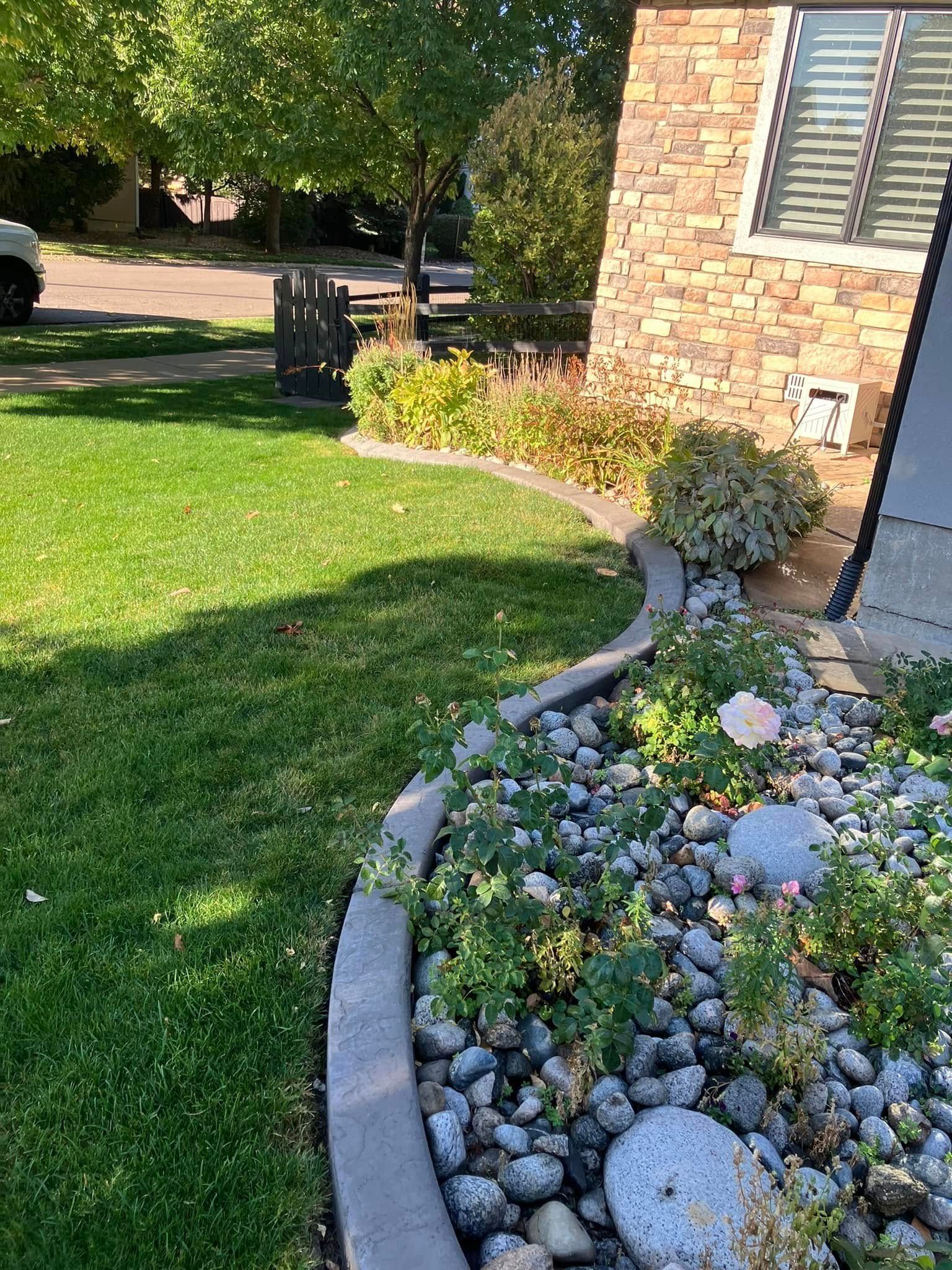 Lawn and garden bed along house with brick veneer and window, bordering a street.