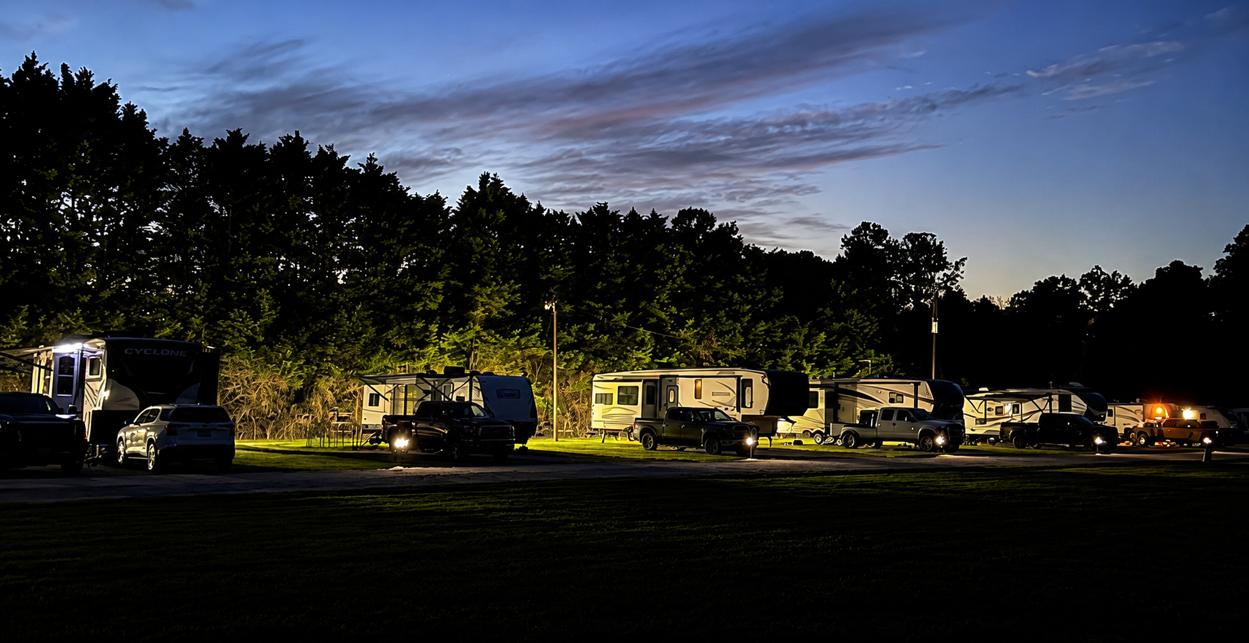 Nighttime RVs and tents lined up in a grassy field under a dusky blue sky.