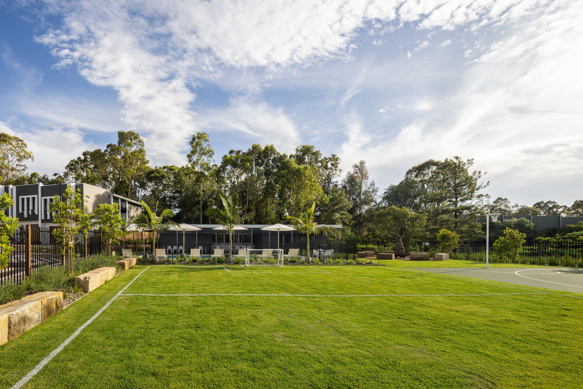 Wide green lawn beside a modern house and trees under a partly cloudy sky