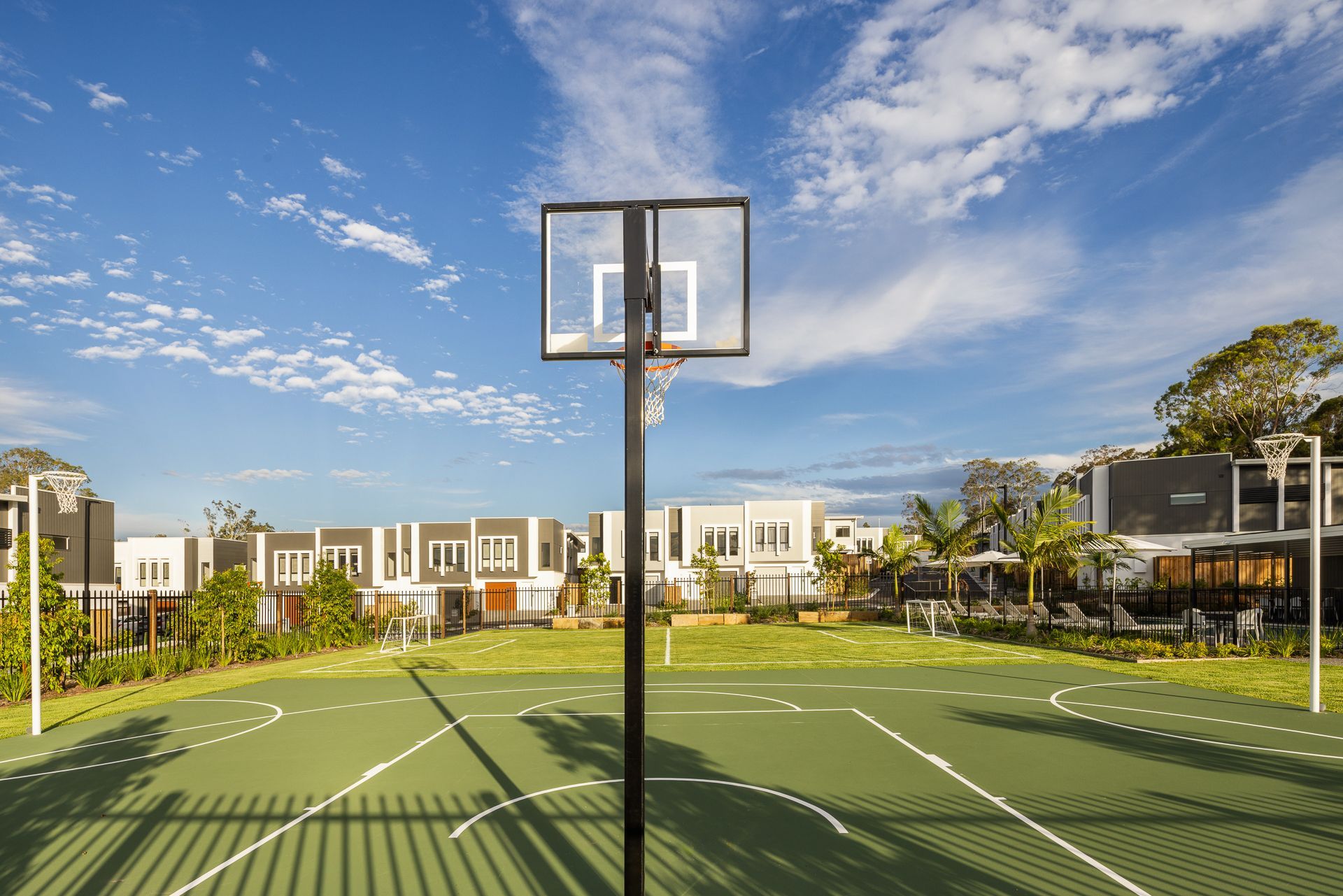 Basketball court with a hoop under a bright blue sky, surrounded by apartment buildings and trees
