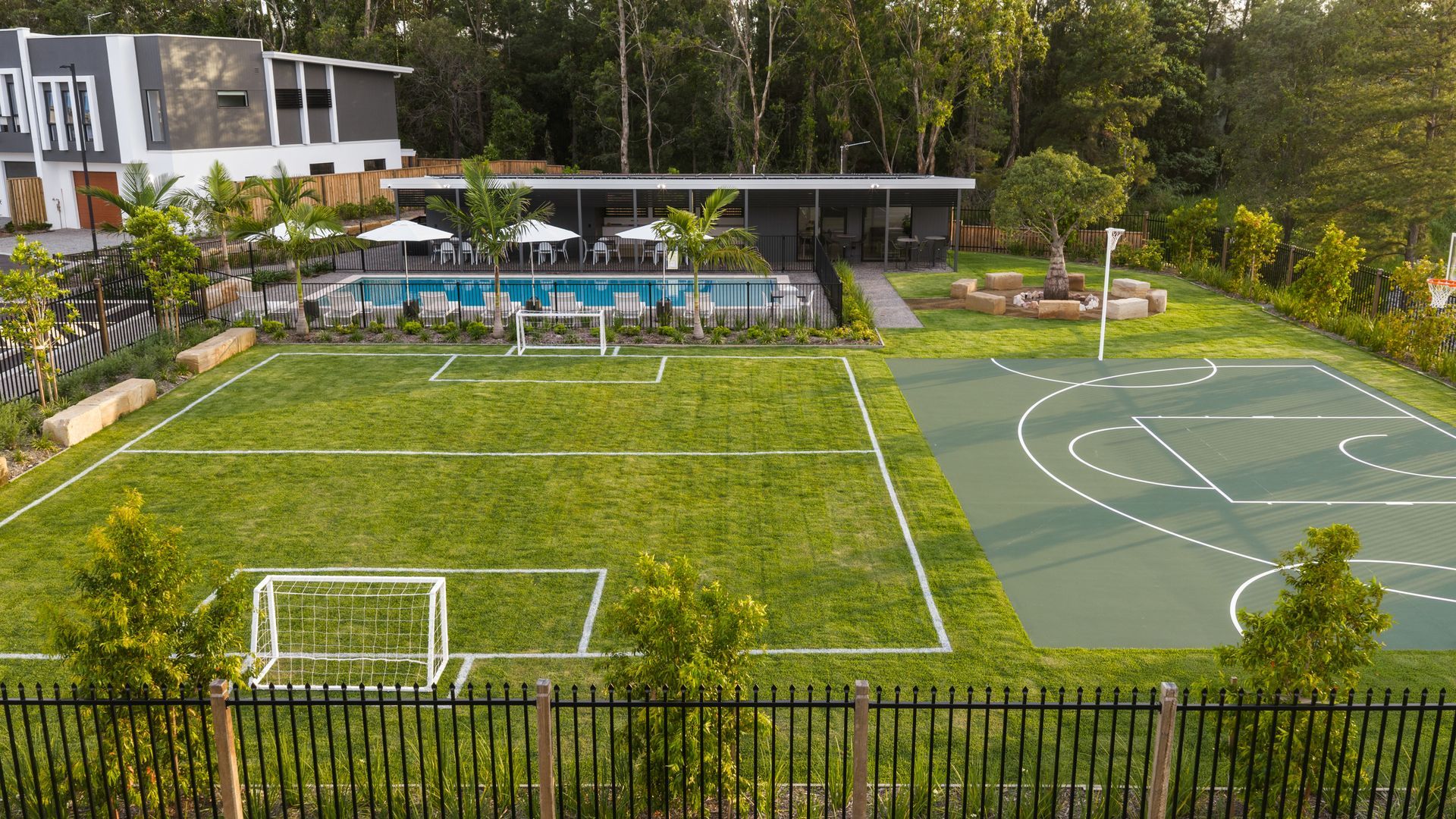 Aerial view of a sports complex with soccer and basketball courts, surrounded by trees and a building.