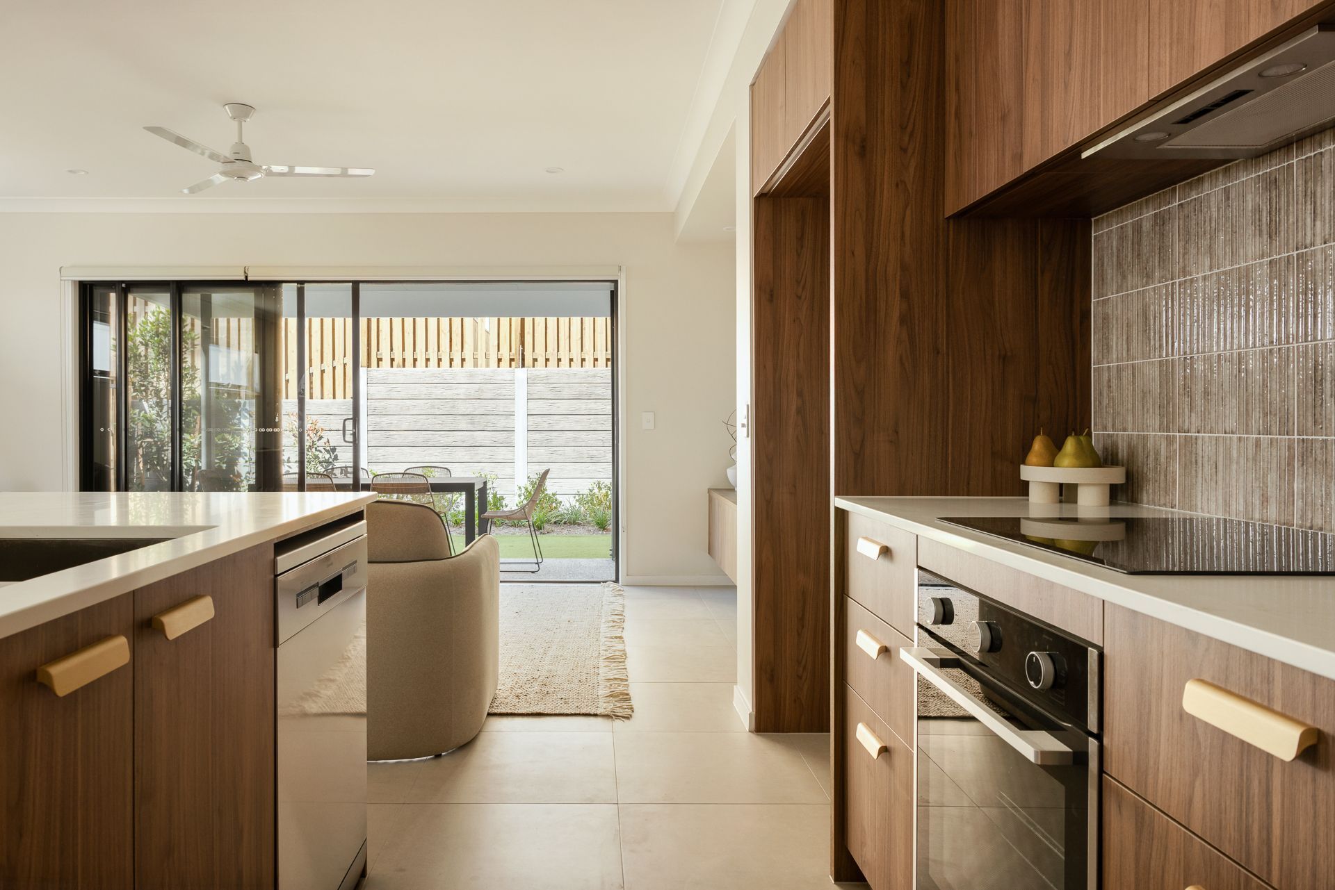 Modern kitchen with wood cabinetry, stone countertop, and open view to a bright patio beyond.