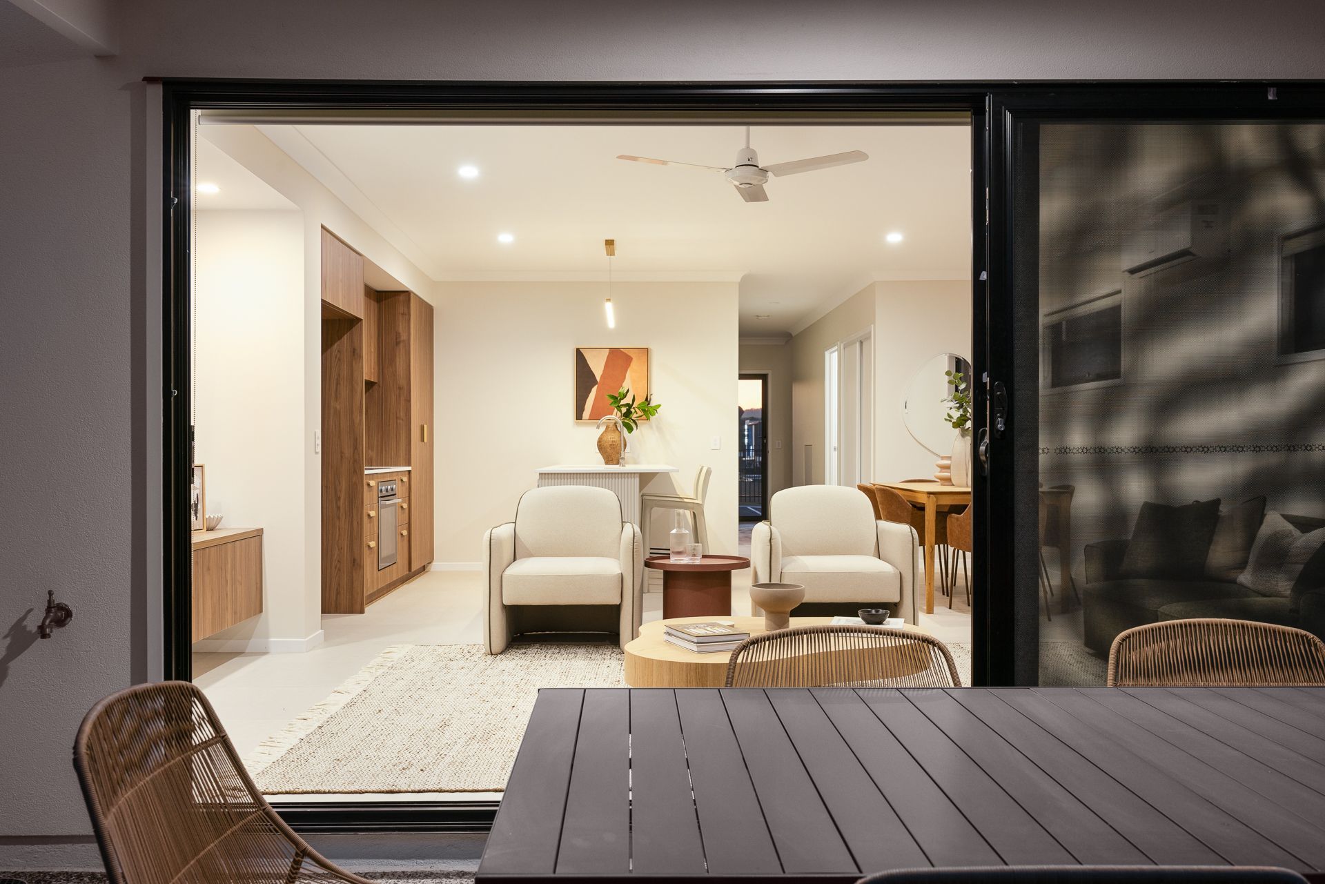 View from patio into a well-lit living room with armchairs, art, and wooden furniture.