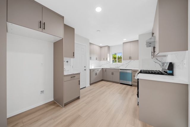 Kitchen with stainless steel range hood above a stovetop, light tile backsplash, and light countertops.