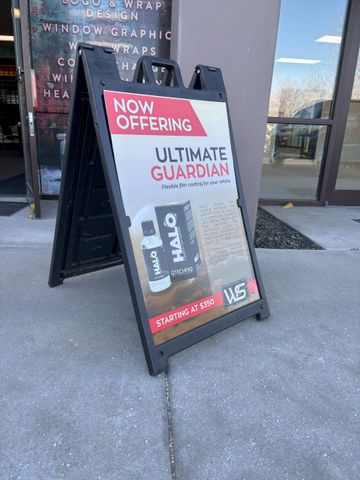 A sign that says `` now offering ultimate guardian '' is sitting on the sidewalk in front of a building.