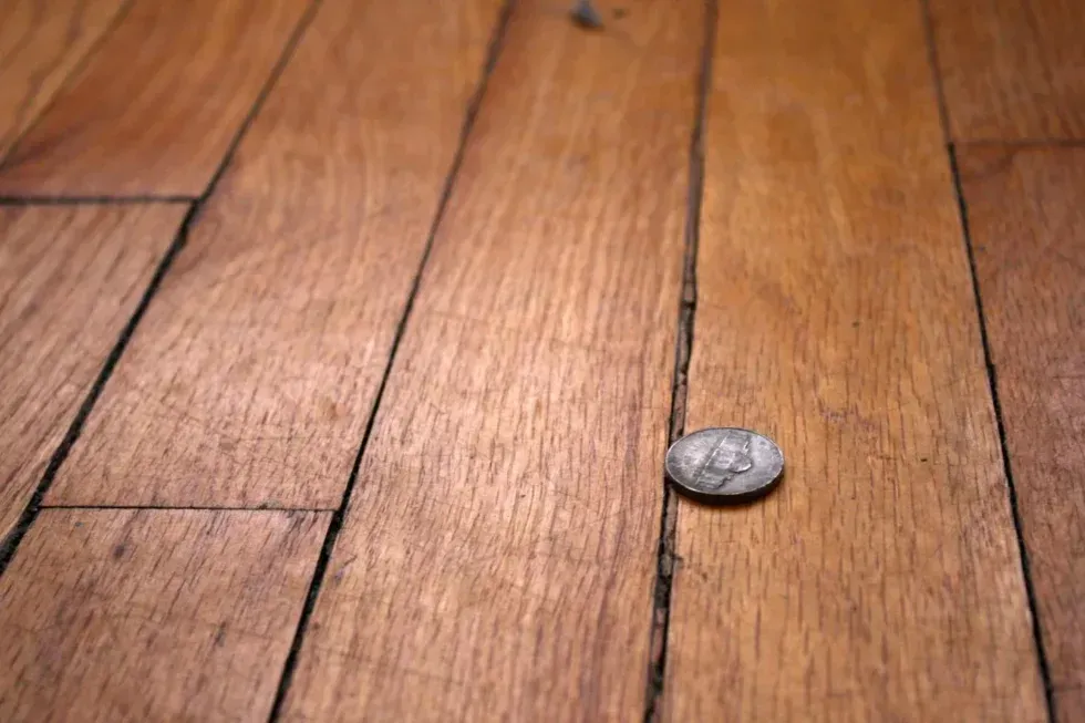 A quarter is sitting on a wooden floor.