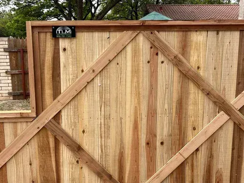 Wooden driveway gate with diagonal braces and a black address plaque in front of a fenced yard