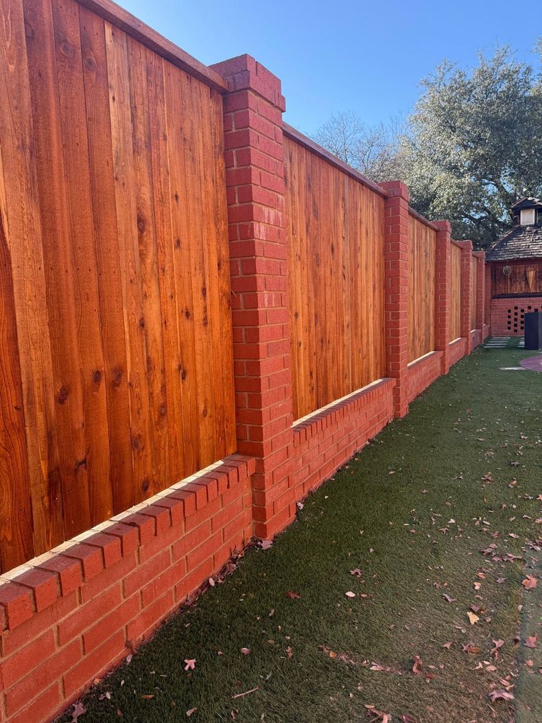 Wooden backyard fence with a metal post, grass, a tree, and houses in the background