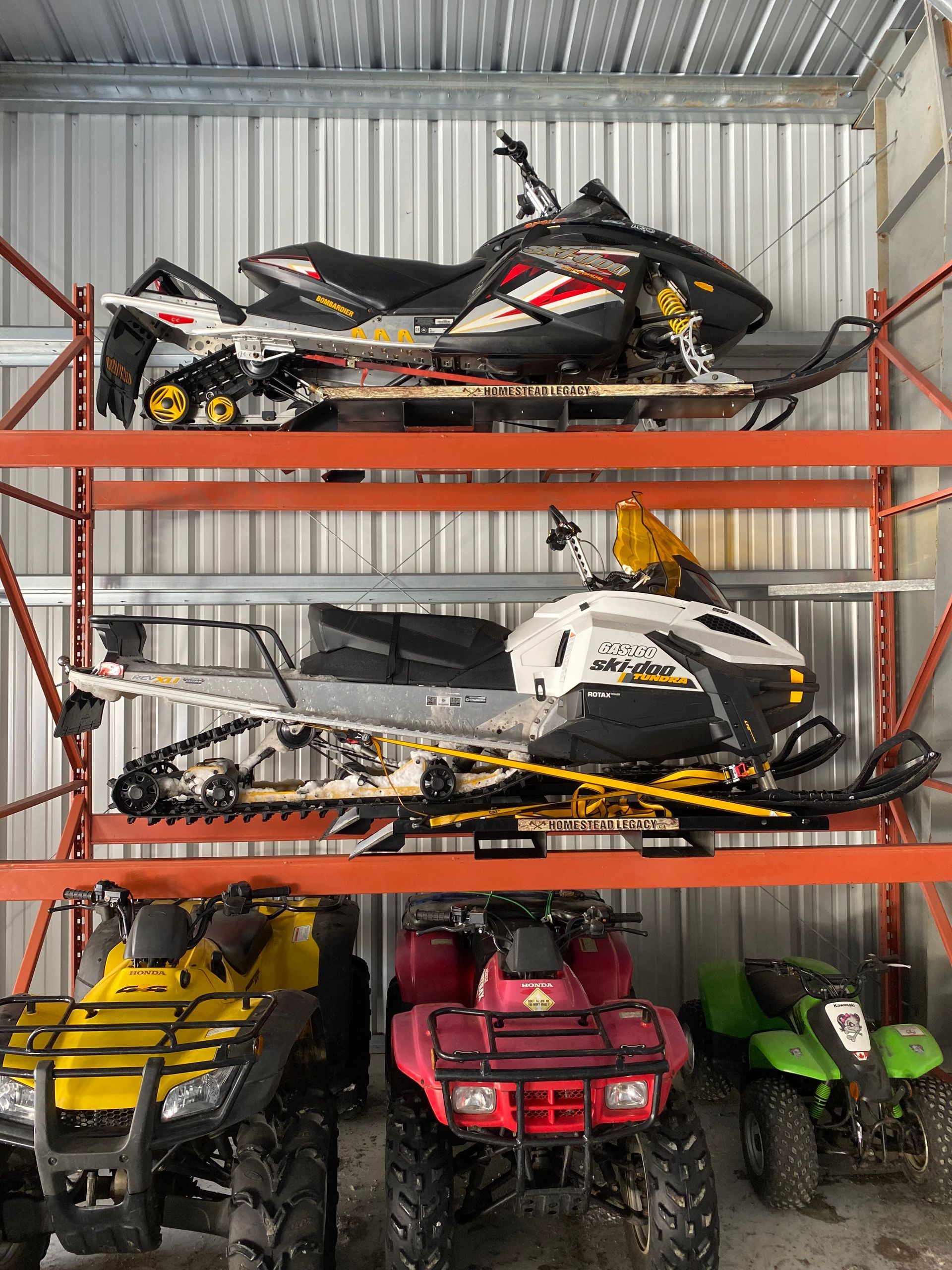 A bunch of snowmobiles are stacked on top of each other in a garage.