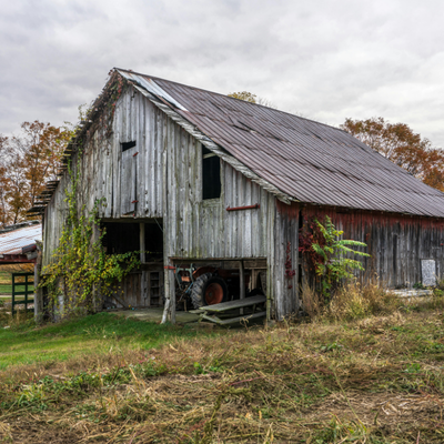 Weathered gray barn with a metal roof in a grassy field under an overcast sky