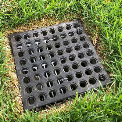 Black rubber utility cover with round holes set in green grass outdoors