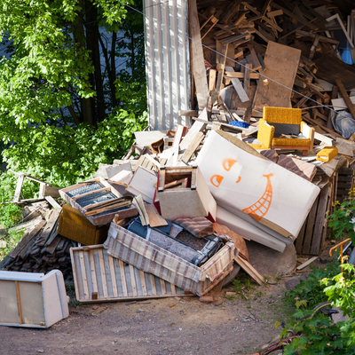 Pile of mixed trash and debris spilling from a metal container beside trees outdoors