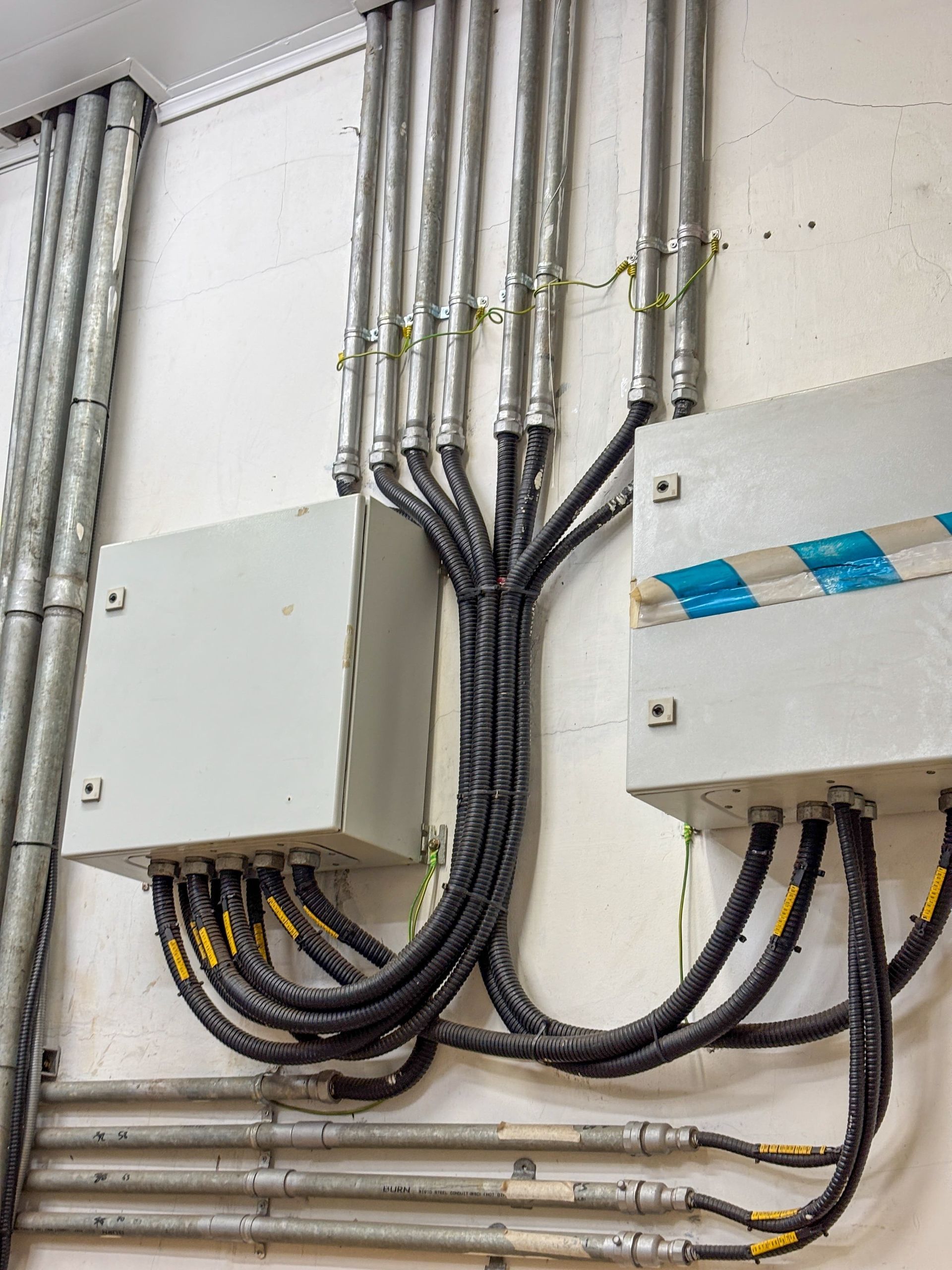 Electrical conduits and black power cables connected to two metal junction boxes mounted on a white wall.
