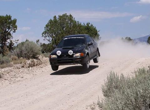Black Subaru rally car airborne on a dirt road, kicking up dust. | Flatout Automotive