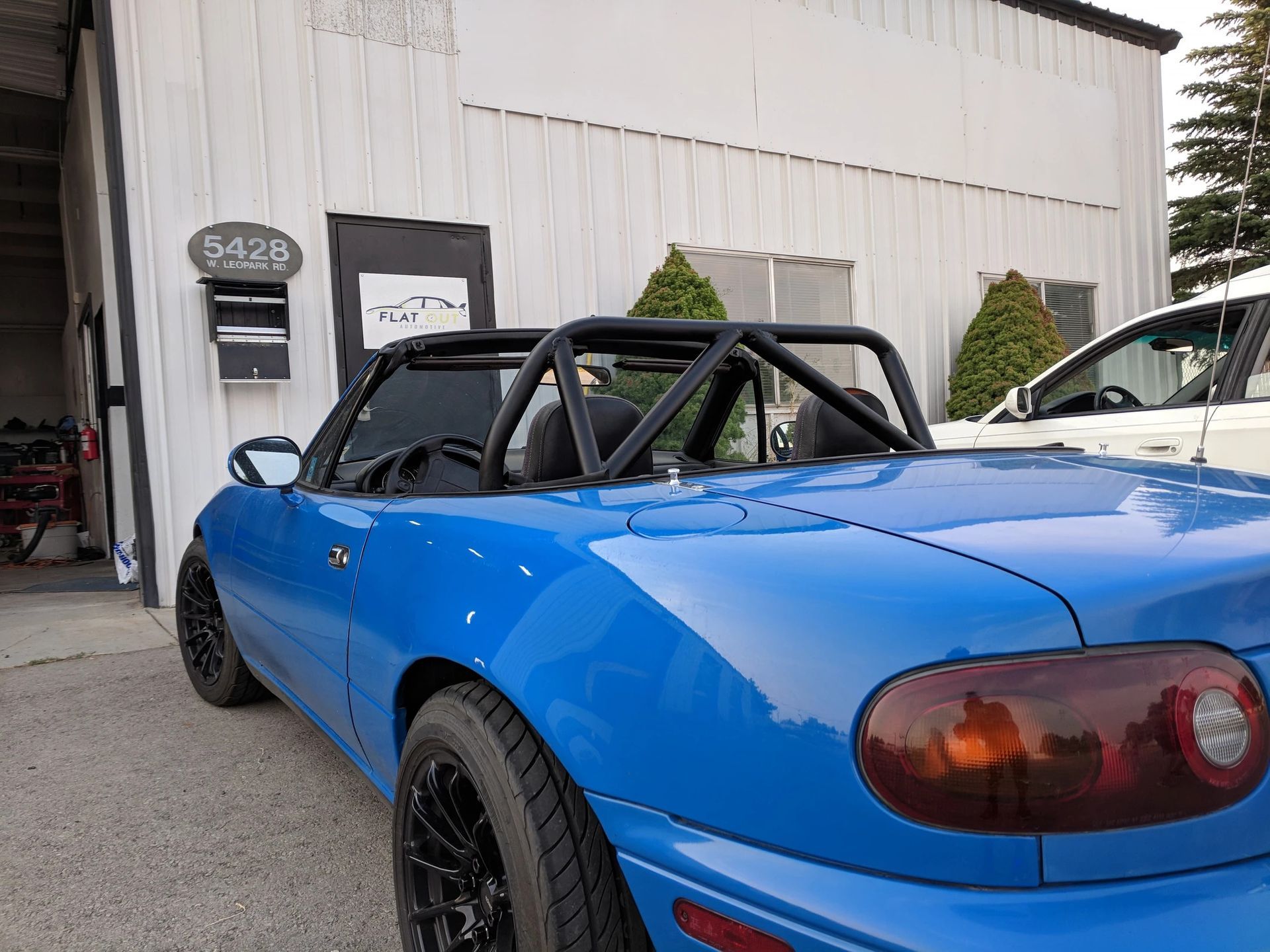 Blue convertible car with black roll bar parked in front of a white building. | Flatout Automotive