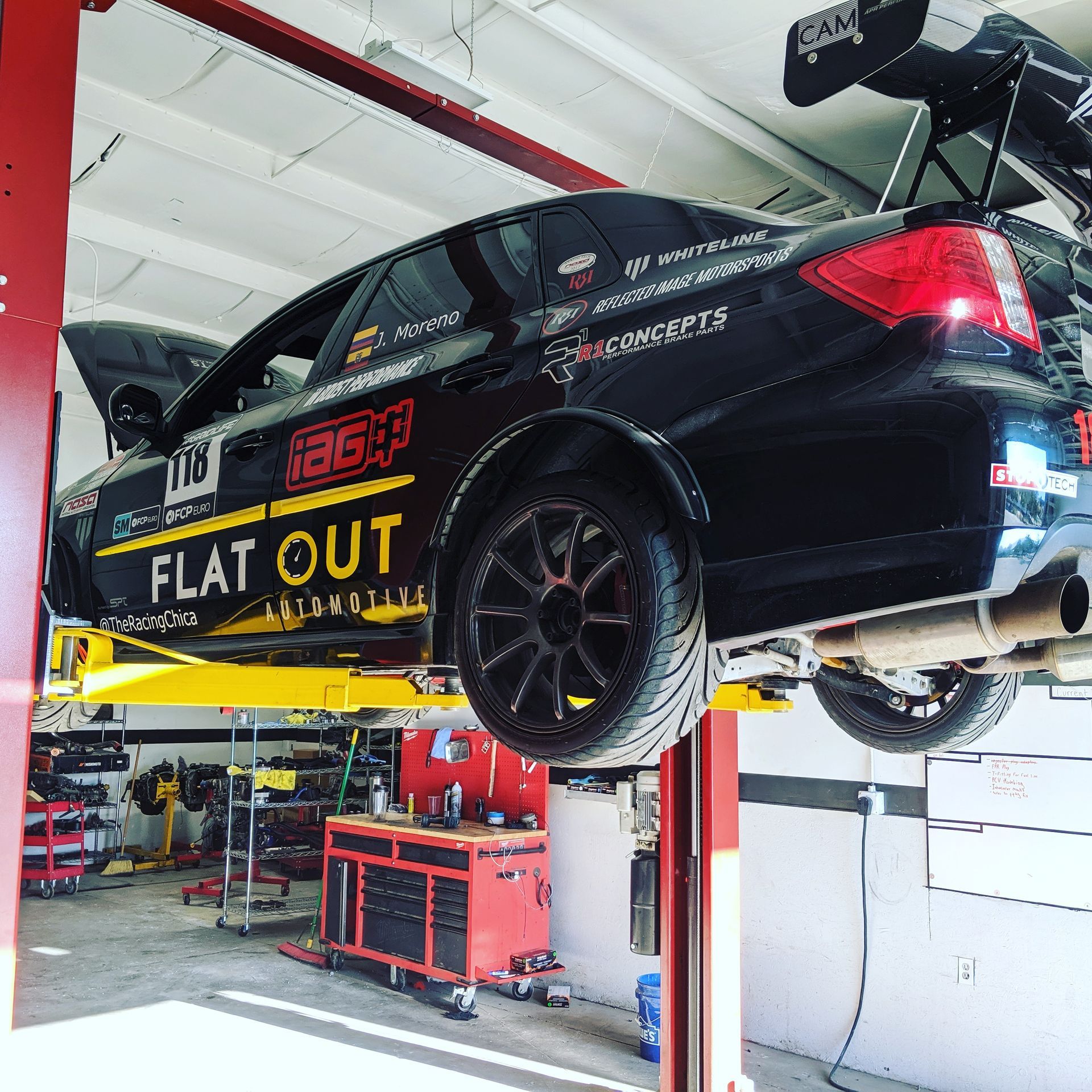 Black race car raised on a lift in a garage, showcasing sponsored branding. | Flatout Automotive