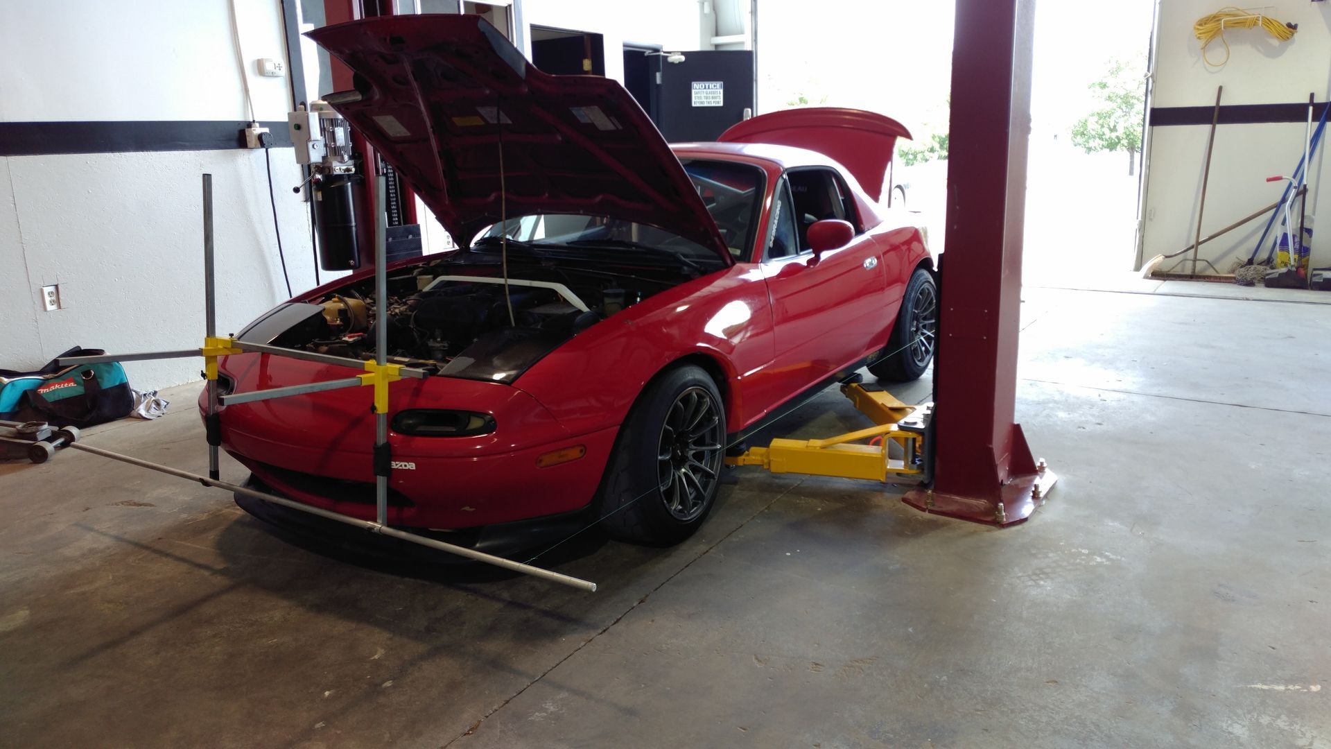 Red convertible car on a lift in a garage with its hood open, being worked on. | Flatout Automotive