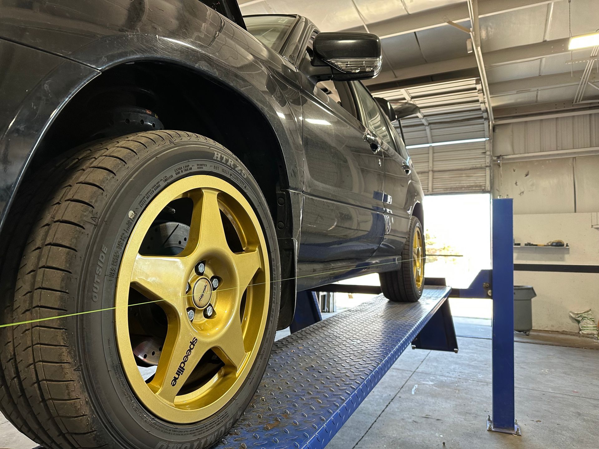 Dark car with gold rims on a lift in a garage. | Flatout Automotive
