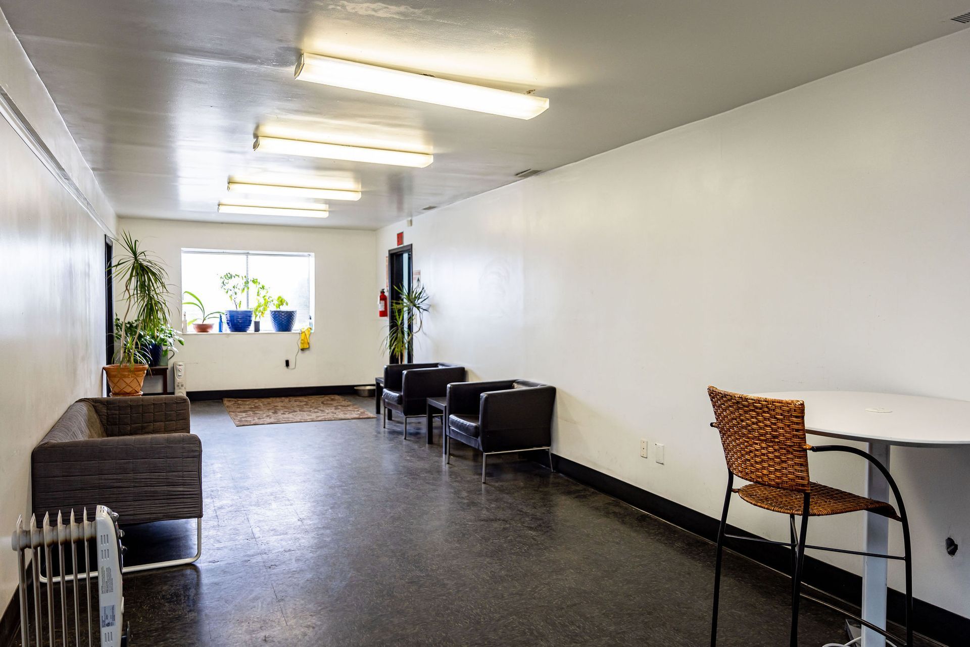 Long, white-walled hallway with a dark floor, seating areas, plants, and fluorescent lights. | Flatout Automotive